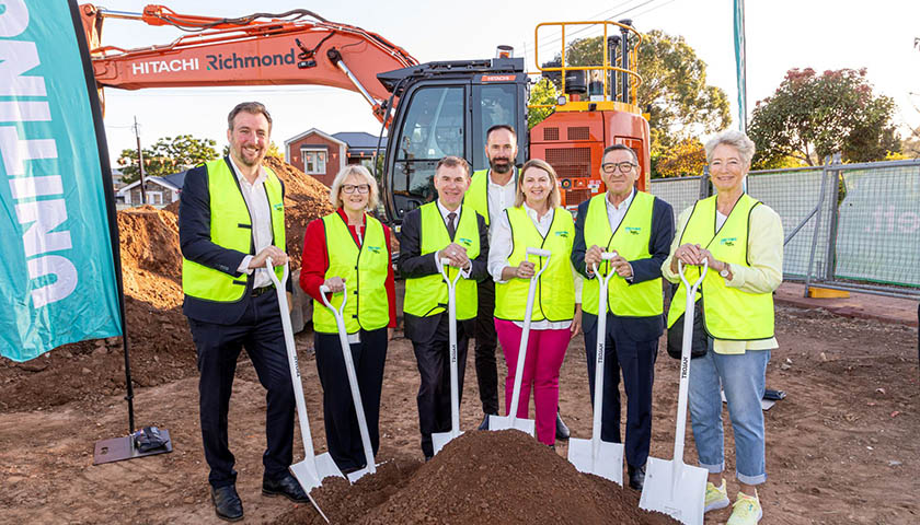 A group of people smiling at the camera and holding shovels digging into the dirt.