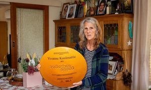Yvonne standing in her living room holding the Red Ochre Prize award.