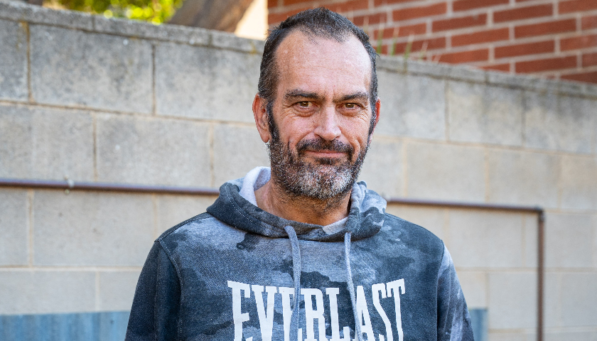 A man wearing a patterned hoodie smiles at the camera.